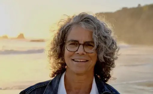 A woman with curly grey hair and glasses on a beach