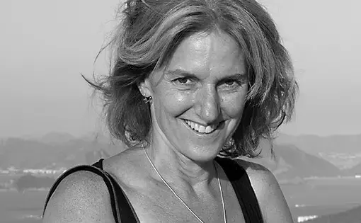 Black and white photo of a woman with shoulder-length hair wearing a black top with a camera strap around her shoulder