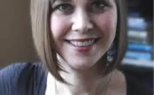 A woman with a short blonde bob with bangs wearing a dark t-shirt
