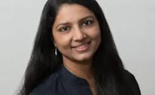 A woman with long dark hair smiles against a neutral background