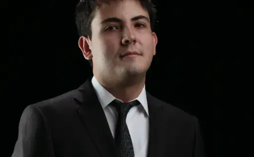 Headshot of a man wearing black suit jacket, white button down, and a black tie