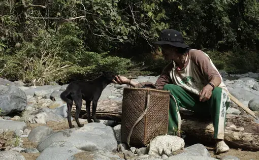 A man pets a black goat in the rocks.
