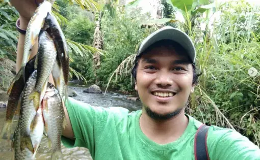 A man wearing a green shirt flashes his teeth as he holds up a bunch of fish in the air.