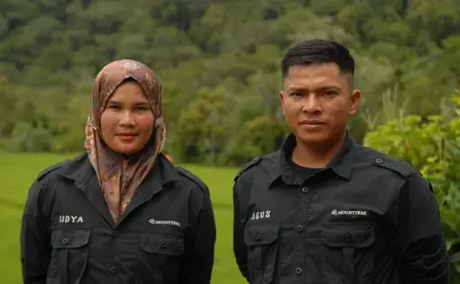 A woman and man stand next to each other, donning black attire, against a green backdrop.