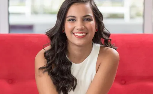 A woman with long dark hair wearing a white top sitting on a red couch