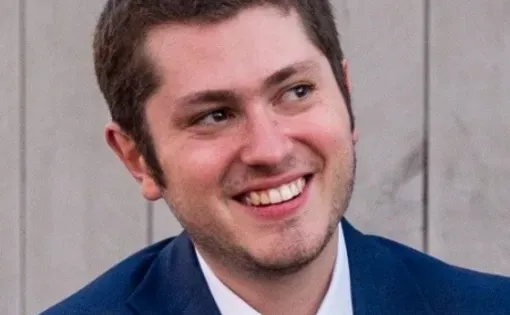 A man with short hair wearing a white button down and blue blazer