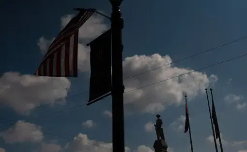 Dark, low-angle image of an American flag blowing on a lamppost