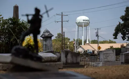 A scene in a small town with a cemetery in the foreground and a church and water tower in the background