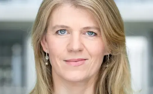 A woman with shoulder-length blonde hair wears a navy patterned blouse