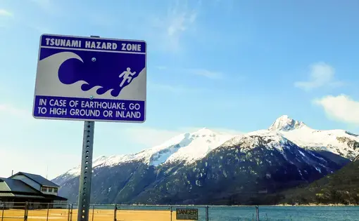 A tsunami warning sign in the foreground against a mountainous background with a lake in between
