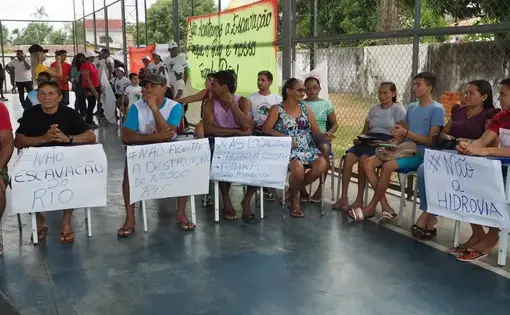 People are seated in protest, holding placards.