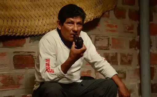A man in white tee sits with  MAPACHO pipe in his hand.