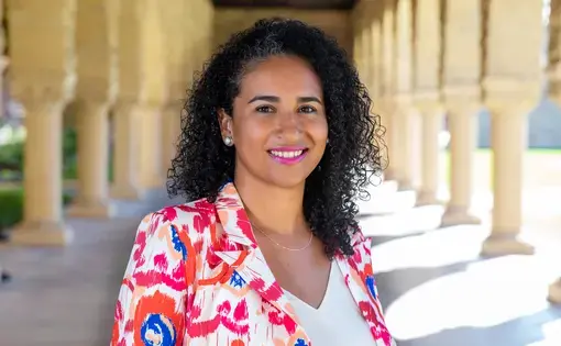 Headshot of a woman with dark curly hair wearing a printed pink and red blazer