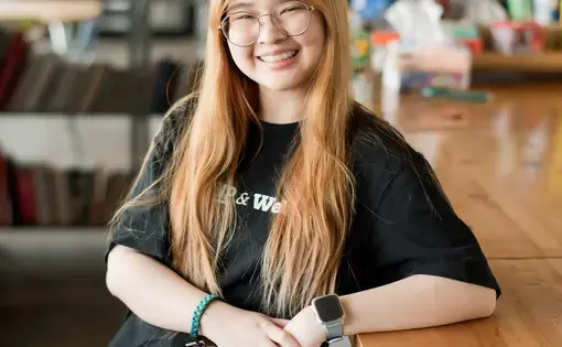 Pitshaya wearing a black tee leans back on a table and smiles into the camera.