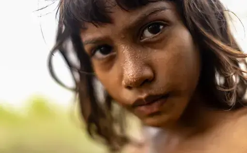 A child peers at the camera with sweat beads dropping from her face.