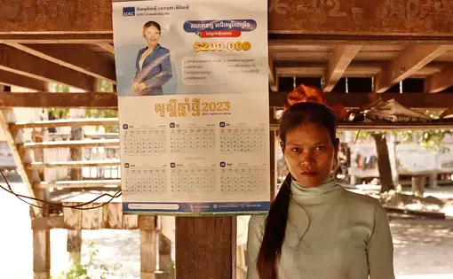 A woman in white pullover stands next to a signboard.