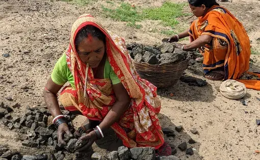 Two women in India kneel around piles of coal
