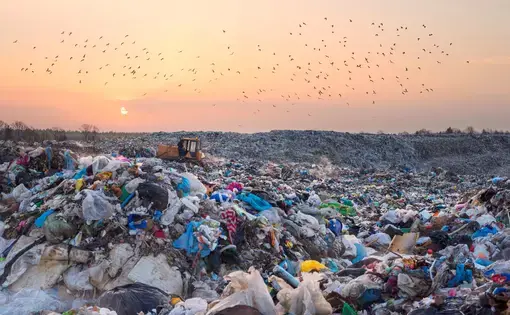 A landfill with an excavator truck in the background at sunset