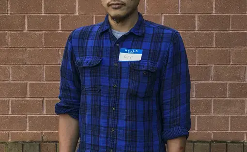 Photo of Go standing against a brick wall wearing a blue button-down