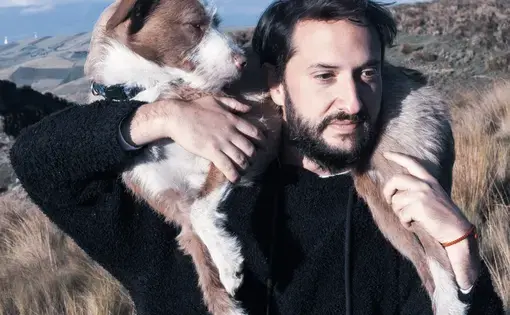 Mijail aA dog is wrapped around Mijail's shoulders against beautiful mountains.