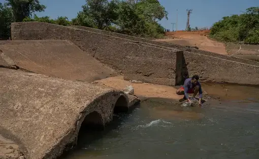 A man sits washing clothes by the river.