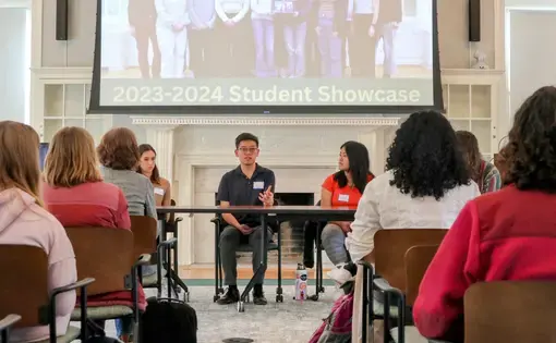 Students present in front of a projector screen to a seated audience
