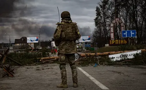A soldier observes the rubble and destroyed vehicles left in a warzone.