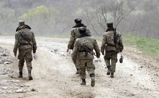 Four soldiers walk down a dirt road