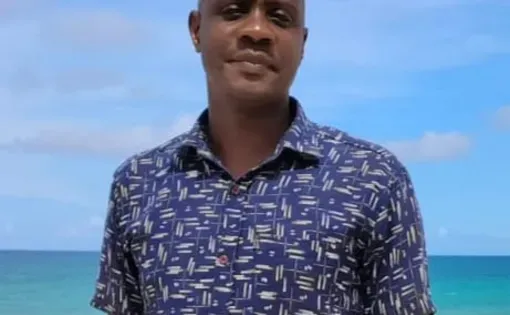 Image of Adrams wearing a blue printed button-down with the ocean in the background