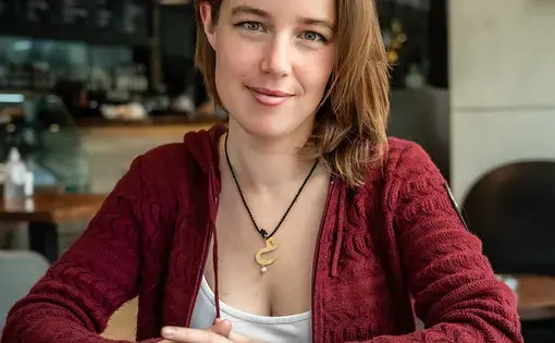 Aisha sits at a table wearing a red cardigan