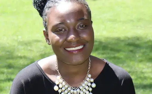 Headshot of Nelly wearing black with a white necklace in a grass field