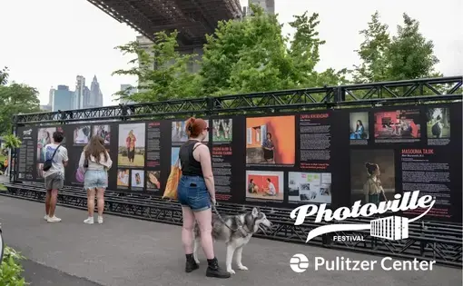 people look at a photography exhibit under the Brooklyn Bridge at Photoville Festival