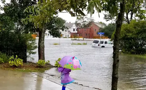 A little girl stands with an umbrella next to a flooded street