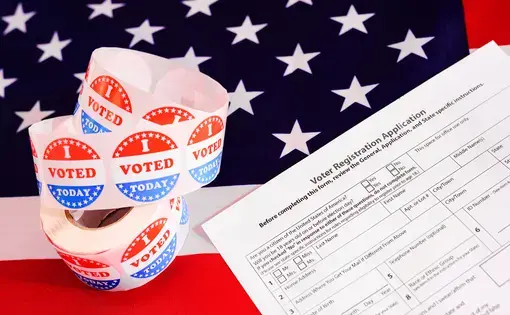 Voter registration form and "I Voted" stickers on top of American flag. Image by Joaquin Corbalan P/Shutterstock.