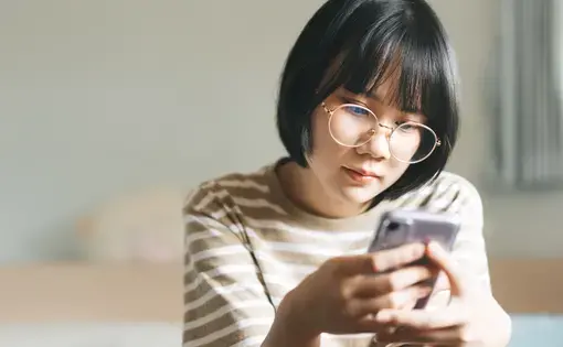A woman looks pensively at her phone. Image by dodotone/Shutterstock.