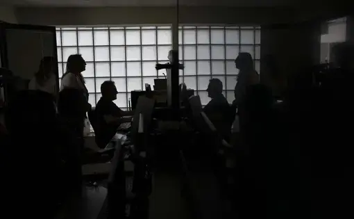 Head of Anti Mafia force (DIA), Carla Durante, left, is silhouetted has she talks with her team in the wire-tape room of the DIA headquarters in Lecce, Italy. Image by Alessandra Tarantino/AP News. Italy, 2024.