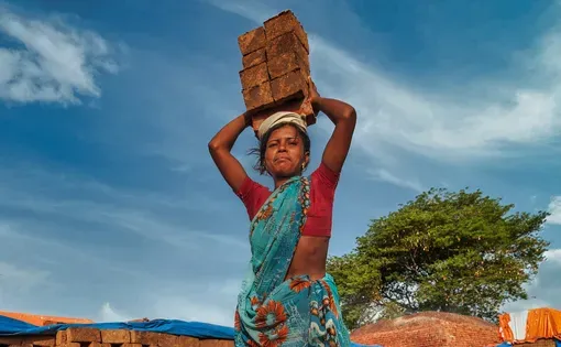 A woman carries a stack of bricks on her head.
