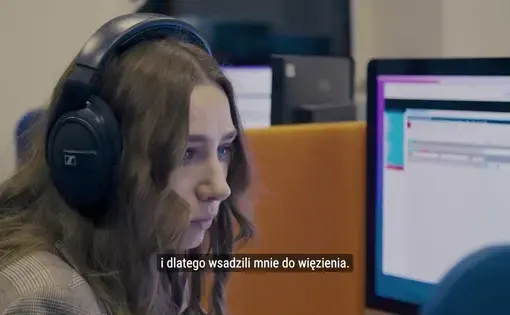 Trailer video thumbnail. A woman with headphones sits at a desk, looks at a screen.