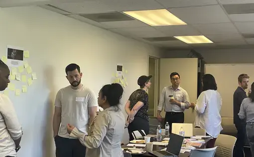 Educators stand next to an image and description of a Pulitzer Center focus issue and engage in a discussion.