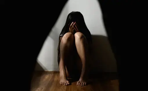 Woman covers her face while sitting on the floor in front of.a white wall
