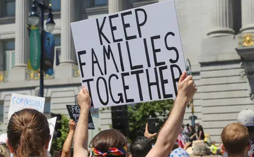 person holds a protest sign that reads "Keep families together"