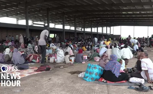 Families are grouped together on mats in a covered area.