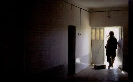 a soldier walks out of a darkened hallway with his back to the photographer