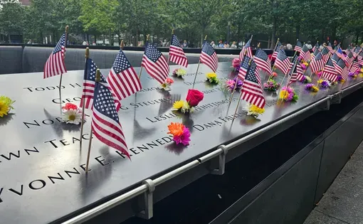 9/11 memomrial monument in New York City with names of people killed, flowers, and American flags