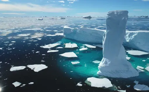 Impressive iceberg melt in the frozen Arctic ocean. Glacier-covered snow drifts under the sunny blue sky. Pure ice floats on turquoise water.