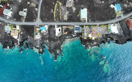 Aerial drone image of a coastline developed with residences, a road, alongside turquoise blue water.