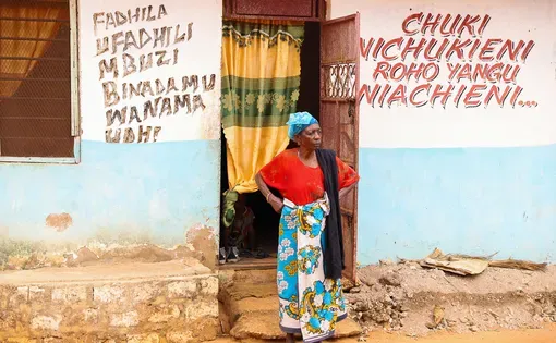 A woman stands outside of a shop, her hands on her knees as she looks down the road