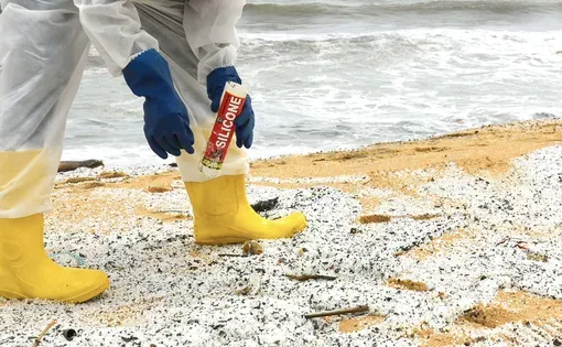 Worker in white protective covering works on a beach