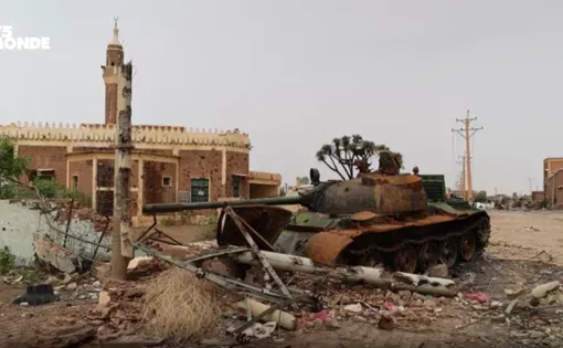 A minaret in the background. A destroyed tank and rubble in the foreground. Image of an urban war zone in Khartoum.