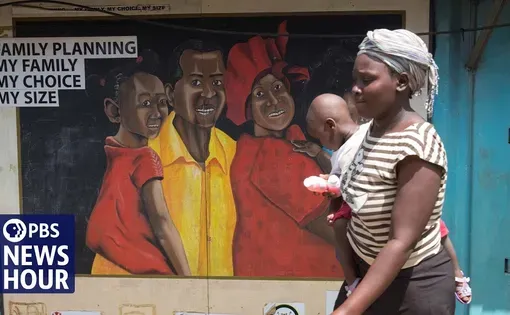 Thumbnail image: A woman carrying a baby walks past a mural of a mother, father, two kids, that says "Family planning, my family, my choice, my size."